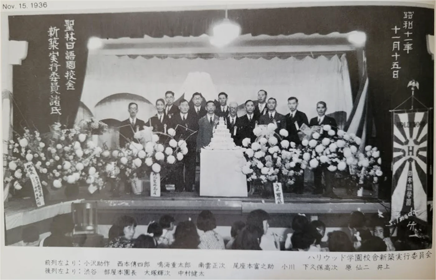 Black-and-white 1936 photograph of the Hollywood Gakuen executive committee gathered on a flower-decorated stage.