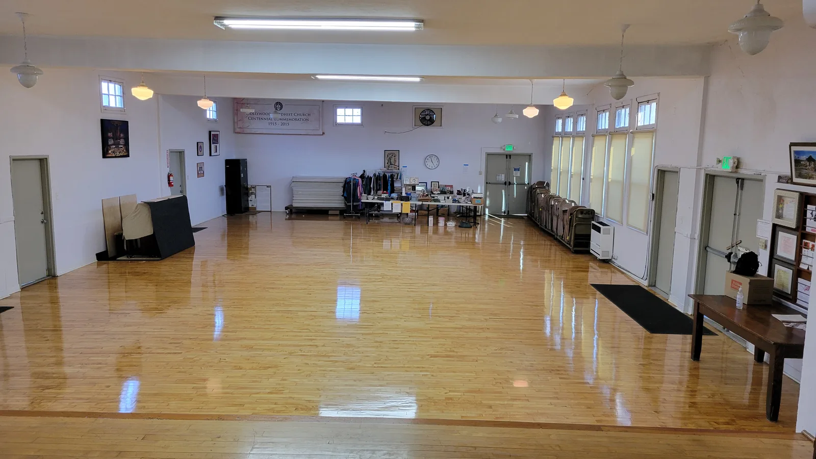 Wide interior view of the HJCI multipurpose hall with its polished hardwood floor, windows, tables, and chairs.